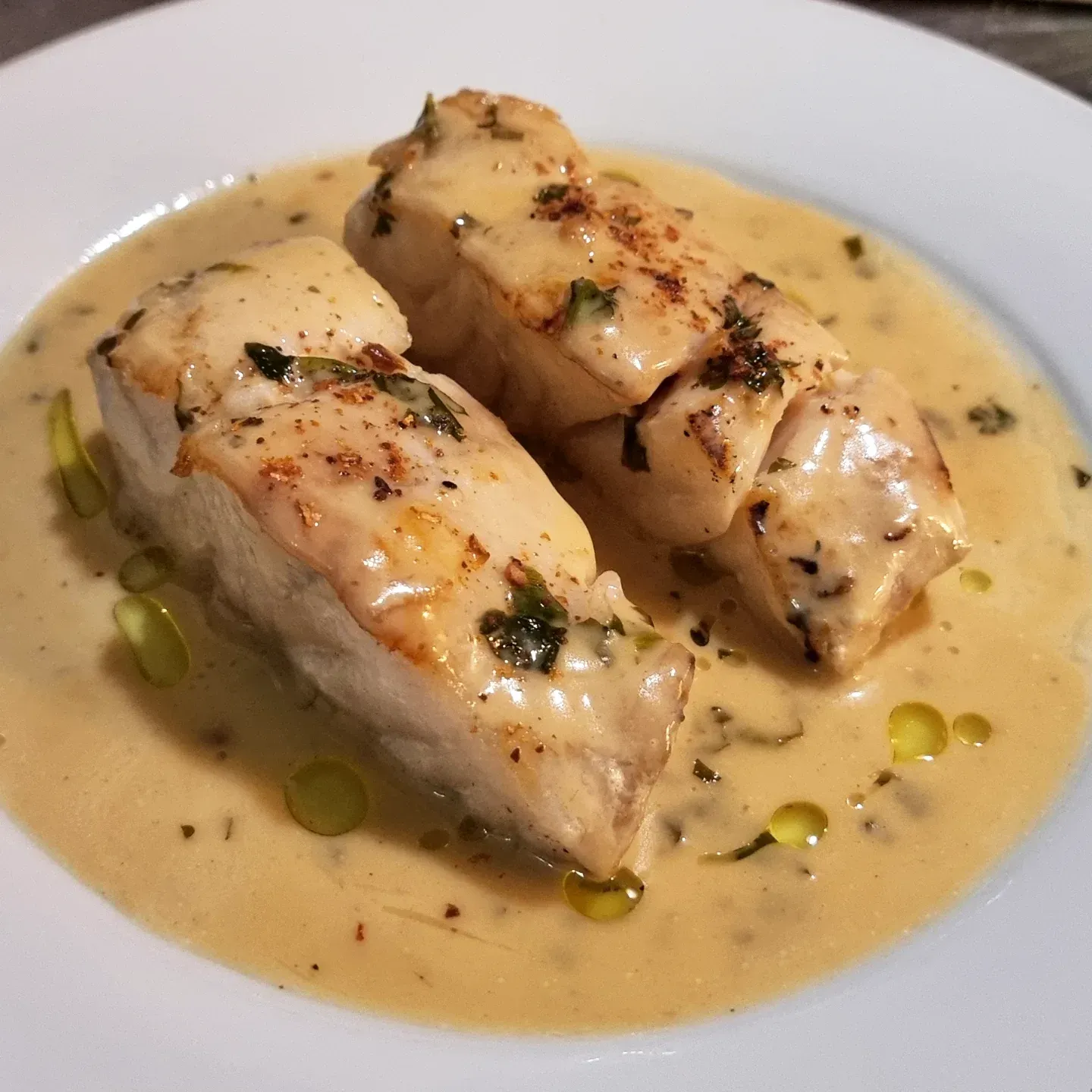 Rollitos de pollo emplatados en salsa cremosa, adornados con hierbas y un chorrito de aceite.