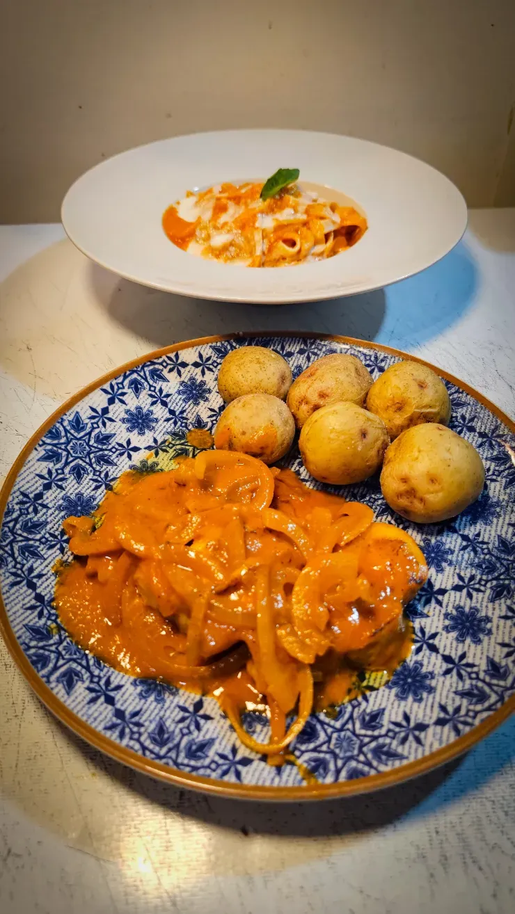 Platos de pasta naranja y patatas cocidas sobre una mesa, con un plato de pasta más pequeño al fondo.