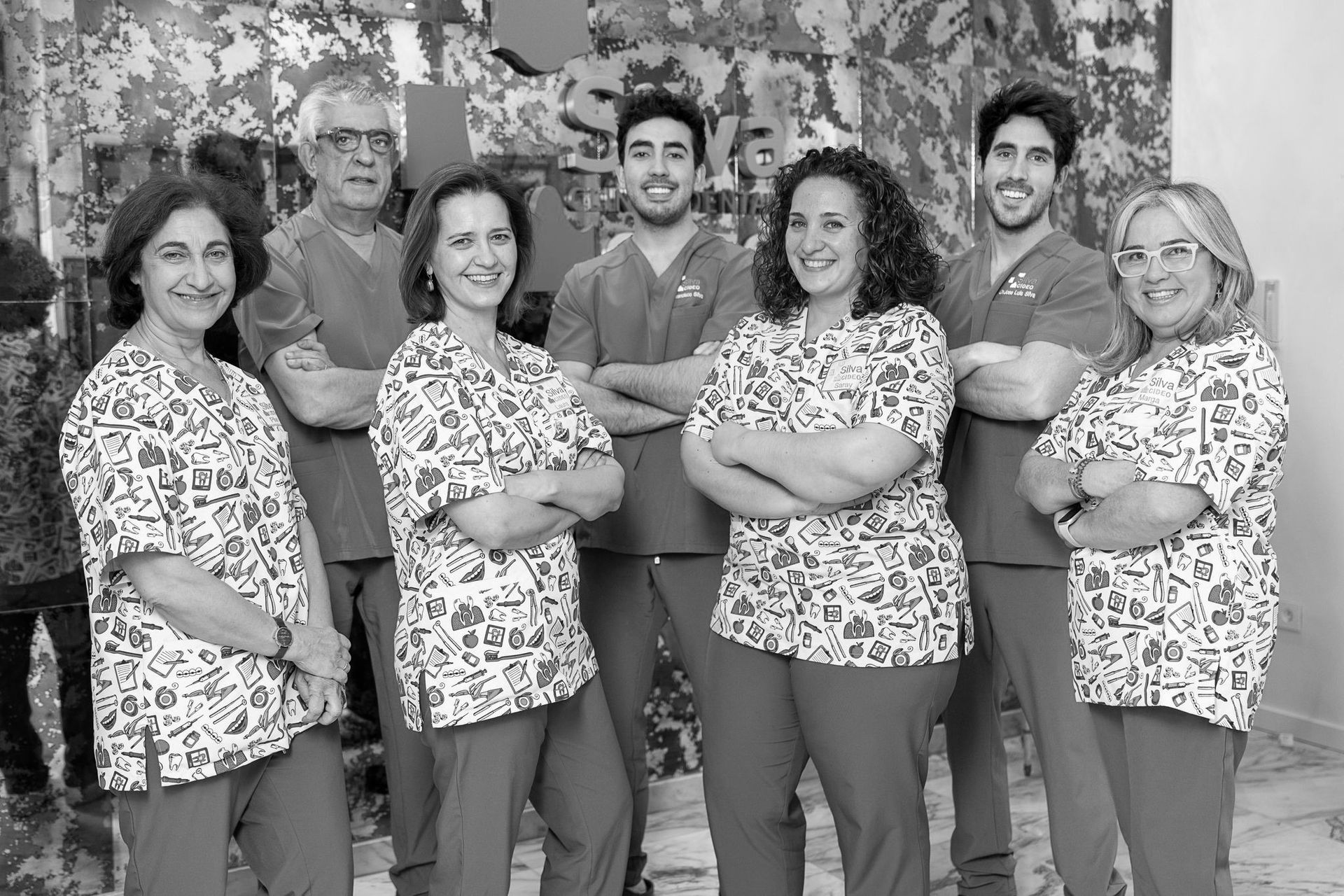 Un grupo de profesionales de la salud, vestidos con uniformes médicos, de pie juntos con los brazos cruzados, en el interior.