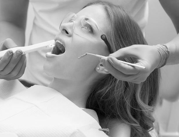 Mujer en la silla del dentista con la boca abierta, siendo examinada con herramientas.