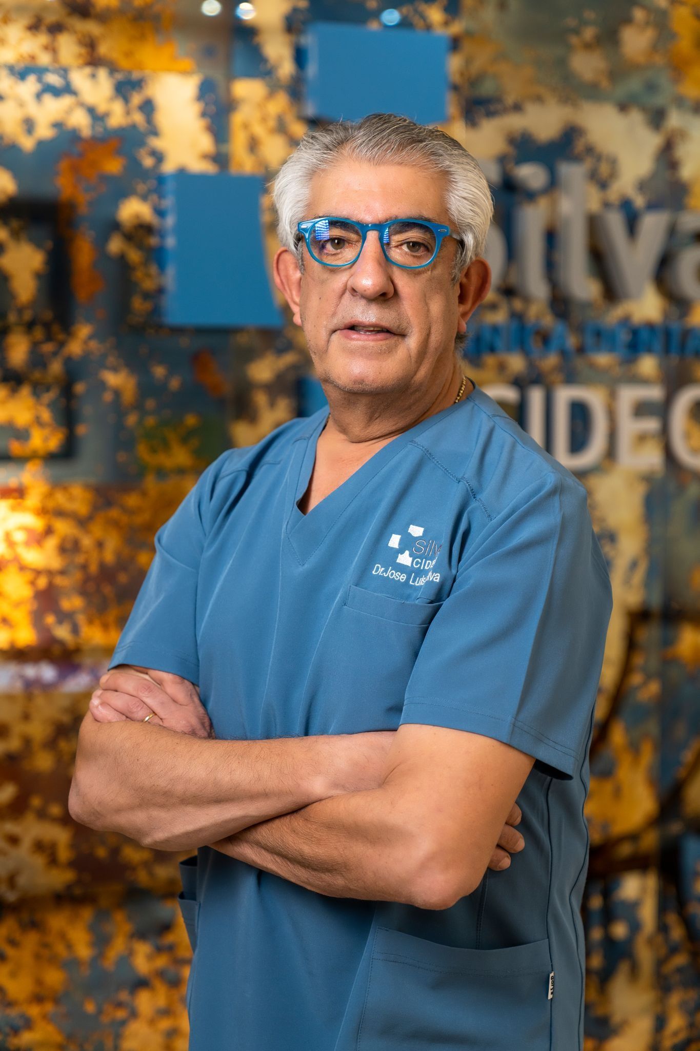 Hombre de pelo gris y gafas con uniforme azul y brazos cruzados.