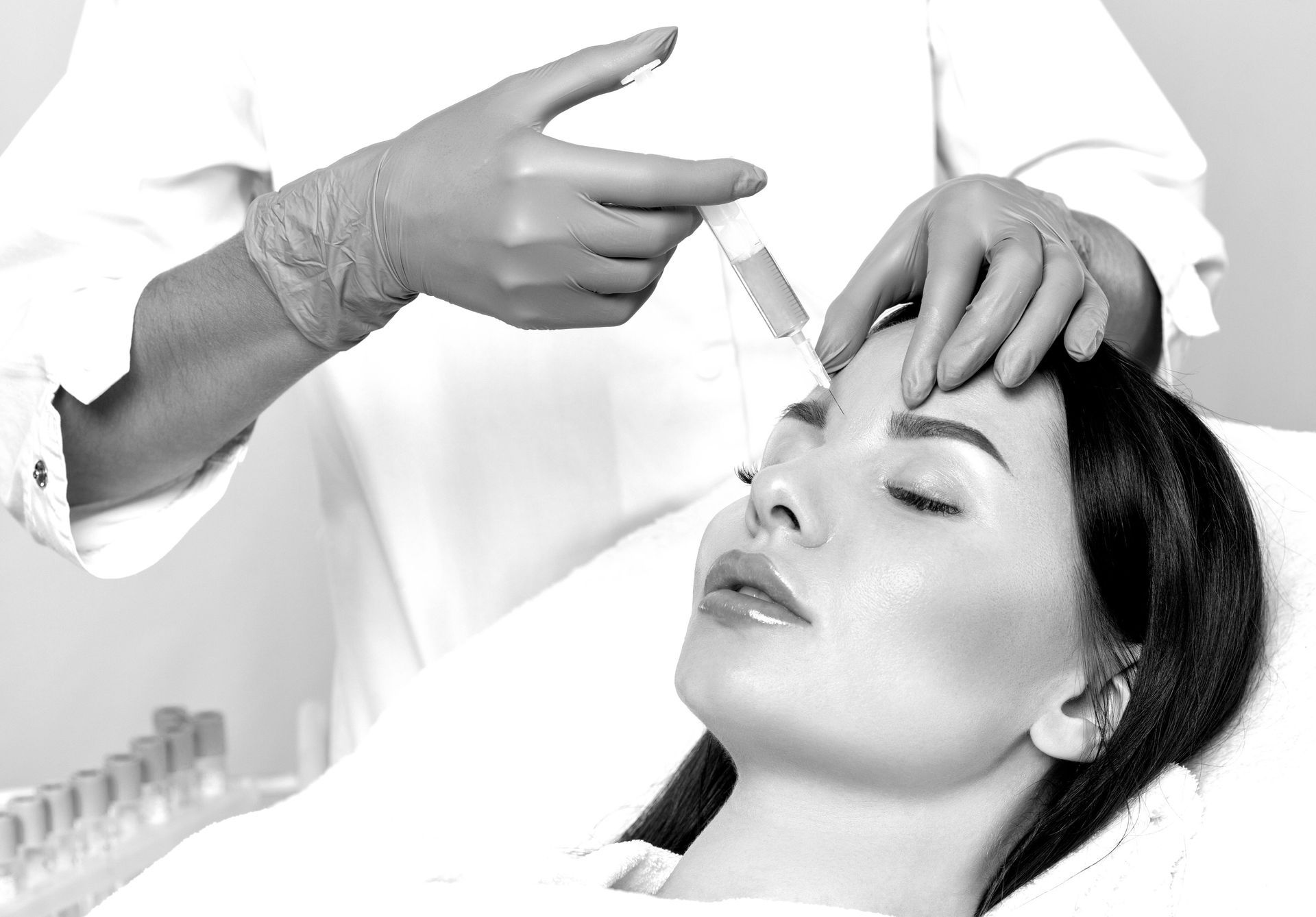 Una persona recibe una inyección facial. Una mano enguantada sostiene una jeringa cerca de la frente.