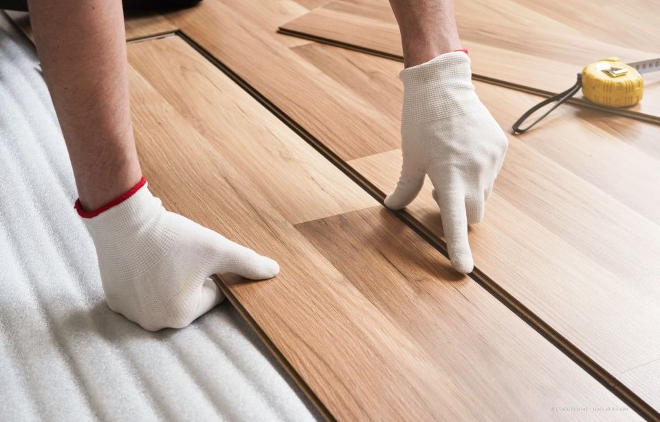 Person mit Handschuhen beim Verlegen von Holzböden.