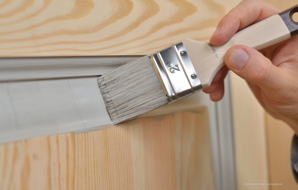 Person streicht eine Türverkleidung mit einem Pinsel weiß.