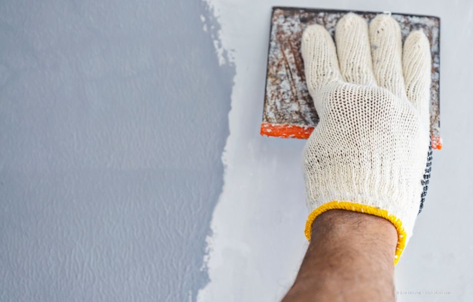 Hand in Handschuh schleift eine gestrichene Wand.