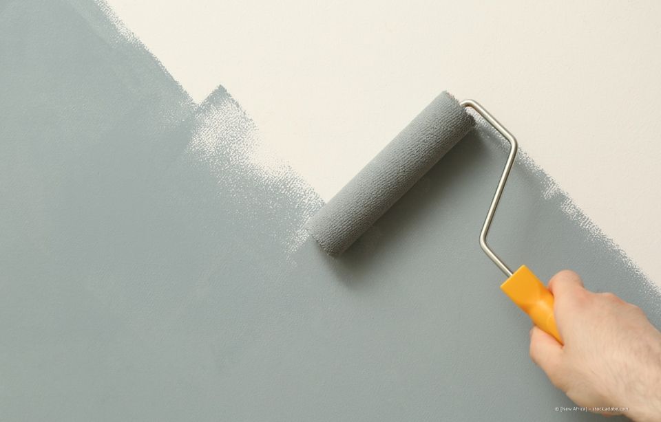 Person, die eine Wand mit einer Farbrolle hellgrau streicht, teilweise Farbdeckung.