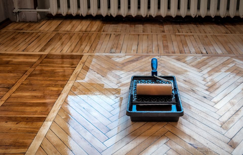 Ein Parkettboden wird mit Rolle und Wanne nachbearbeitet. Holzdielen, helle und dunkle Flecken.