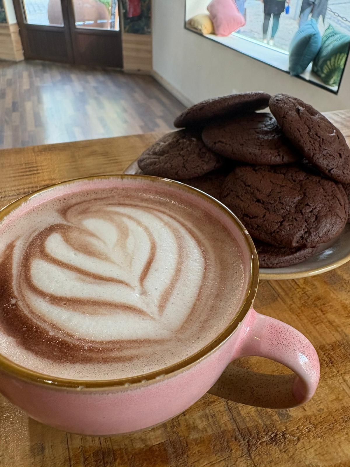 Taza de café con leche de color rosa con diseño de corazón y galletas de chocolate en un plato.