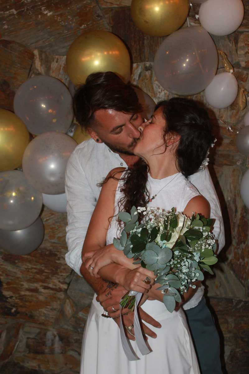 Pareja besándose, mujer sosteniendo ramo, rodeada de globos; celebrando en el interior.