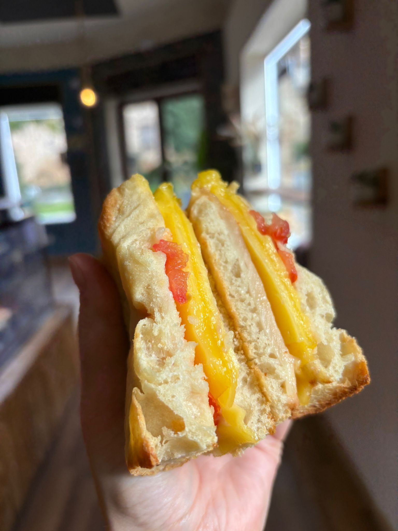 Mano sosteniendo un sándwich, cortado por la mitad, mostrando el relleno amarillo con rodajas de tomate rojo.