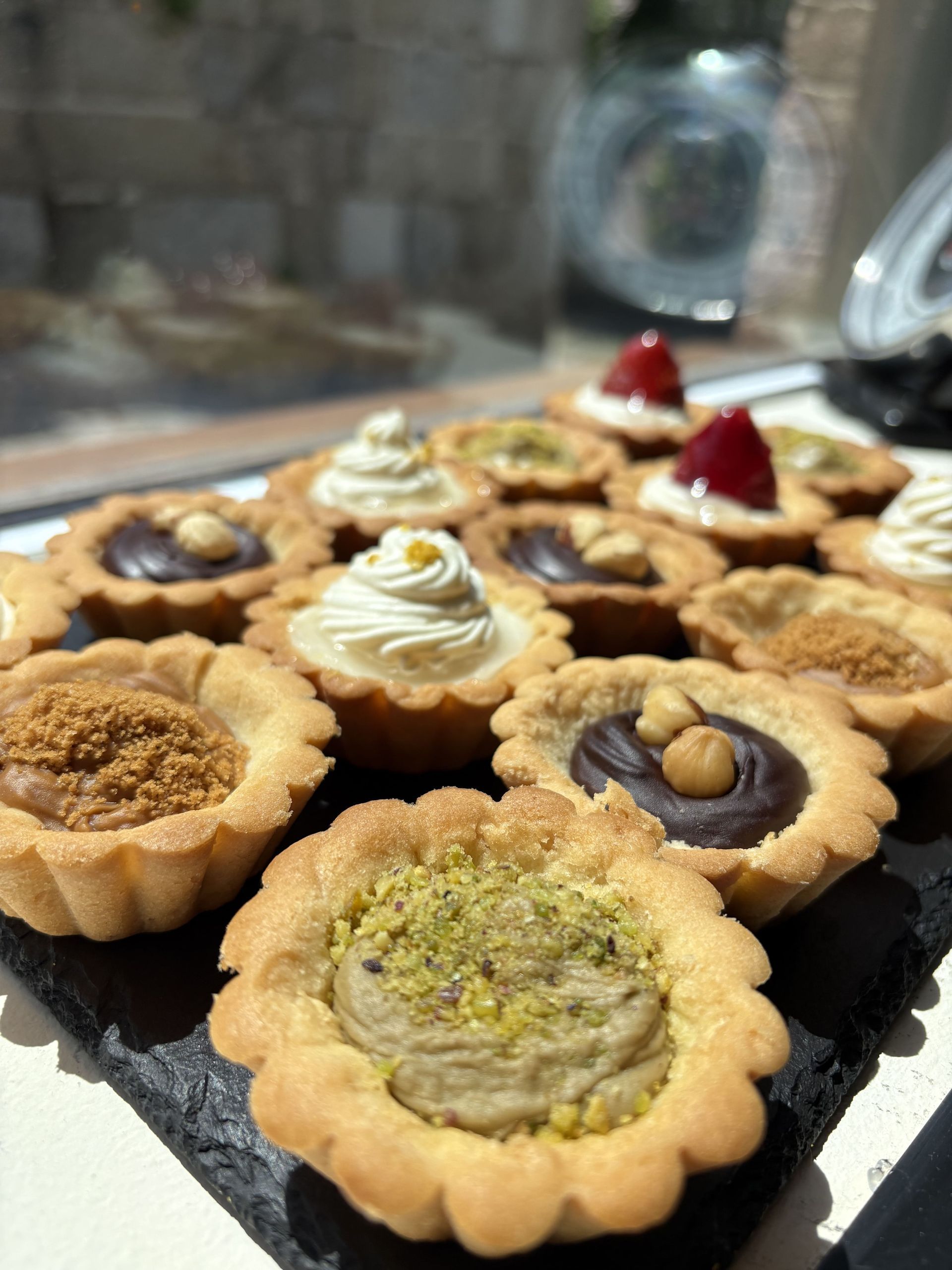 Mini tartas sobre pizarra negra, cada una con diferentes ingredientes como chocolate, nueces y frutas.