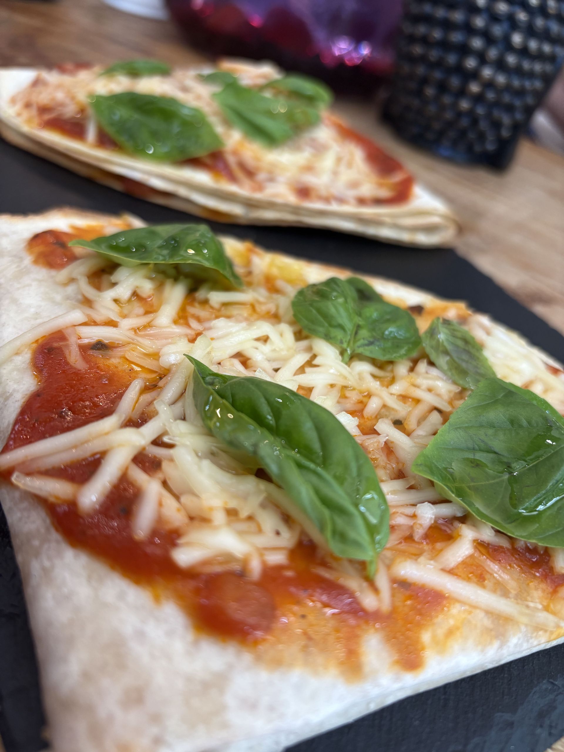 Pizzas de tortilla con salsa de tomate, queso rallado y hojas de albahaca sobre una superficie negra.