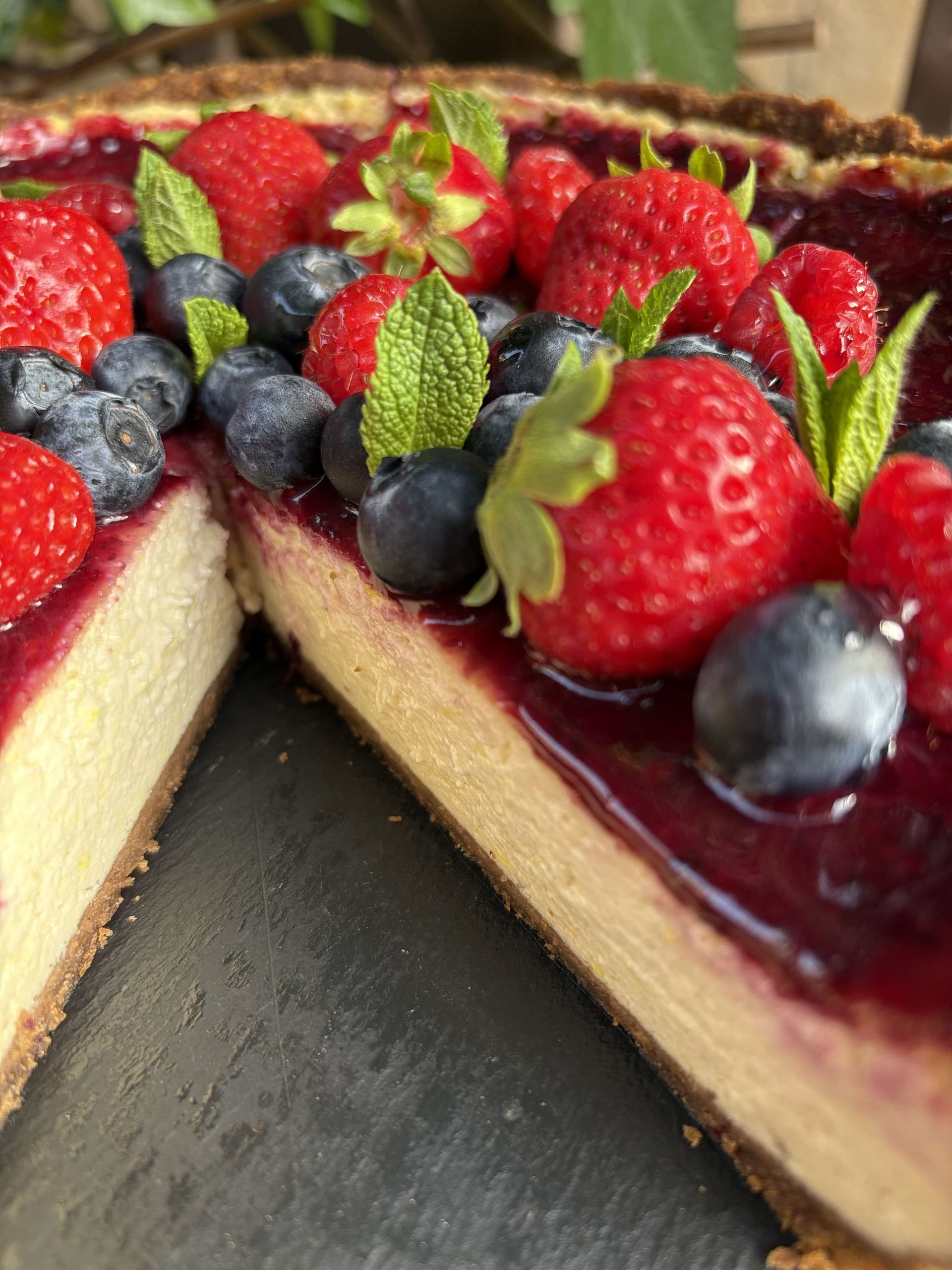 Tarta de queso con cobertura de frutos rojos y adornada con menta.