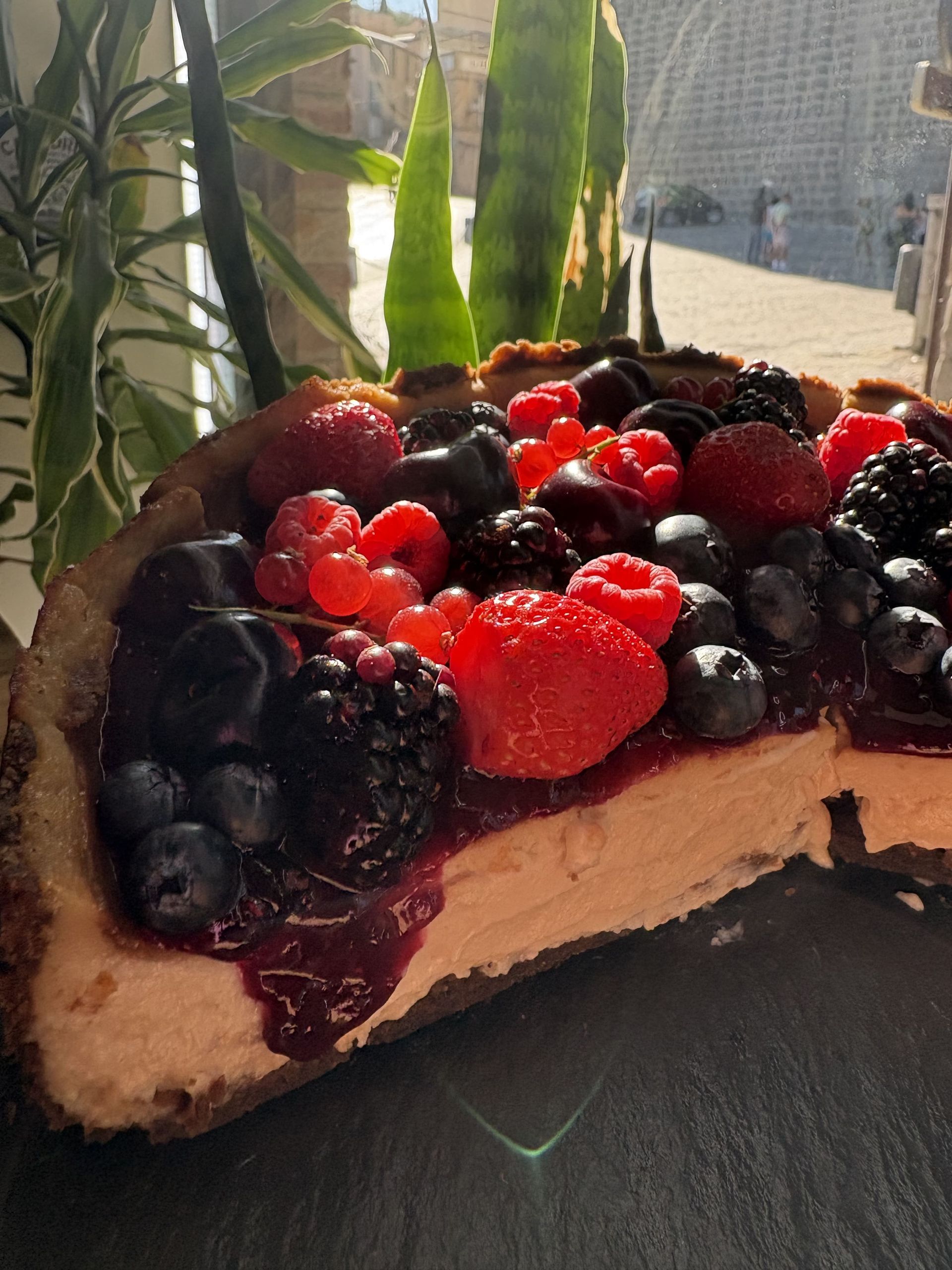 Rebanada de tarta de queso cubierta con frutos rojos mixtos, corteza oscura y relleno cremoso.