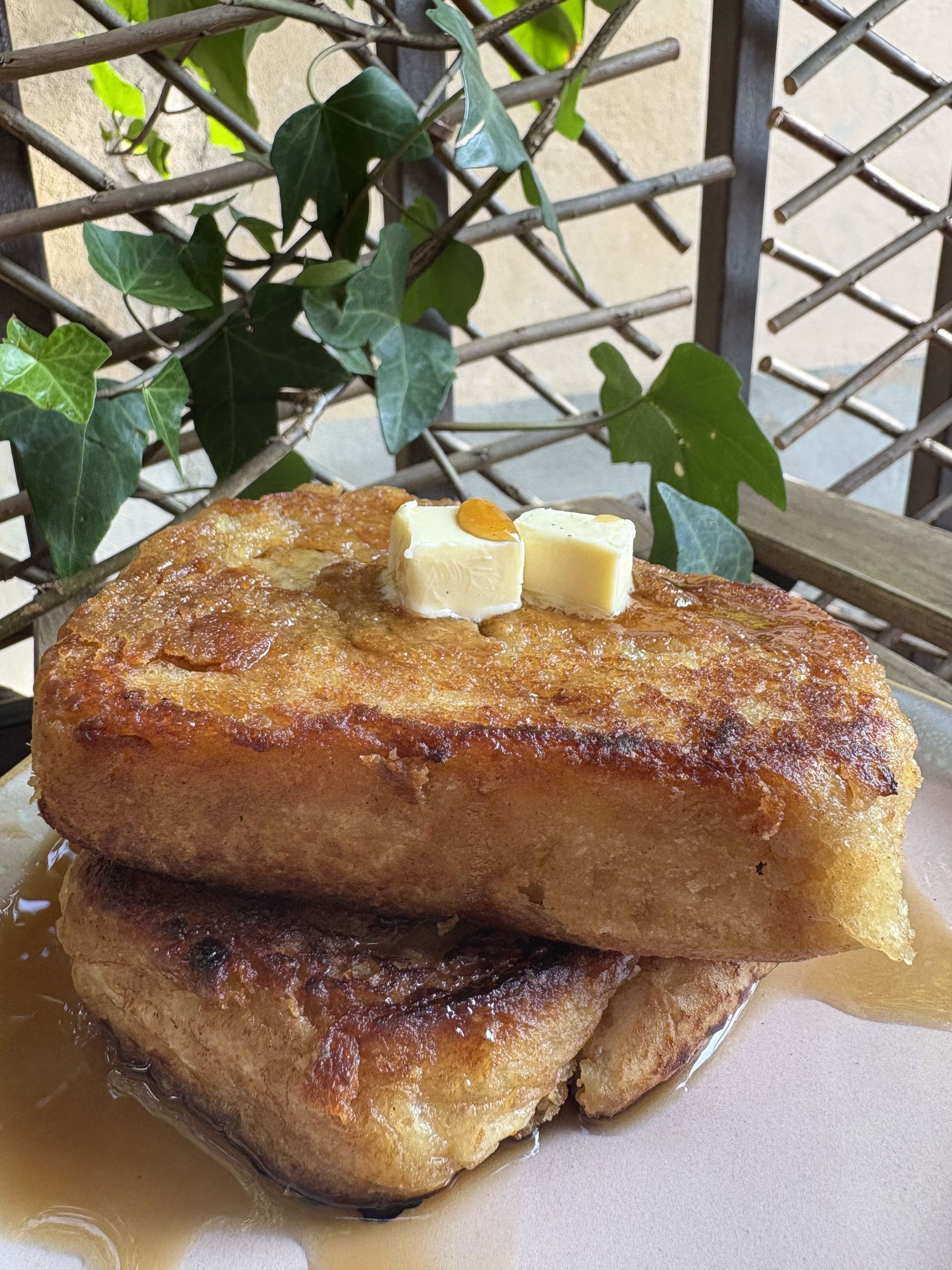 Tostada francesa con mantequilla y sirope, apiladas en un plato. Hiedra al fondo.