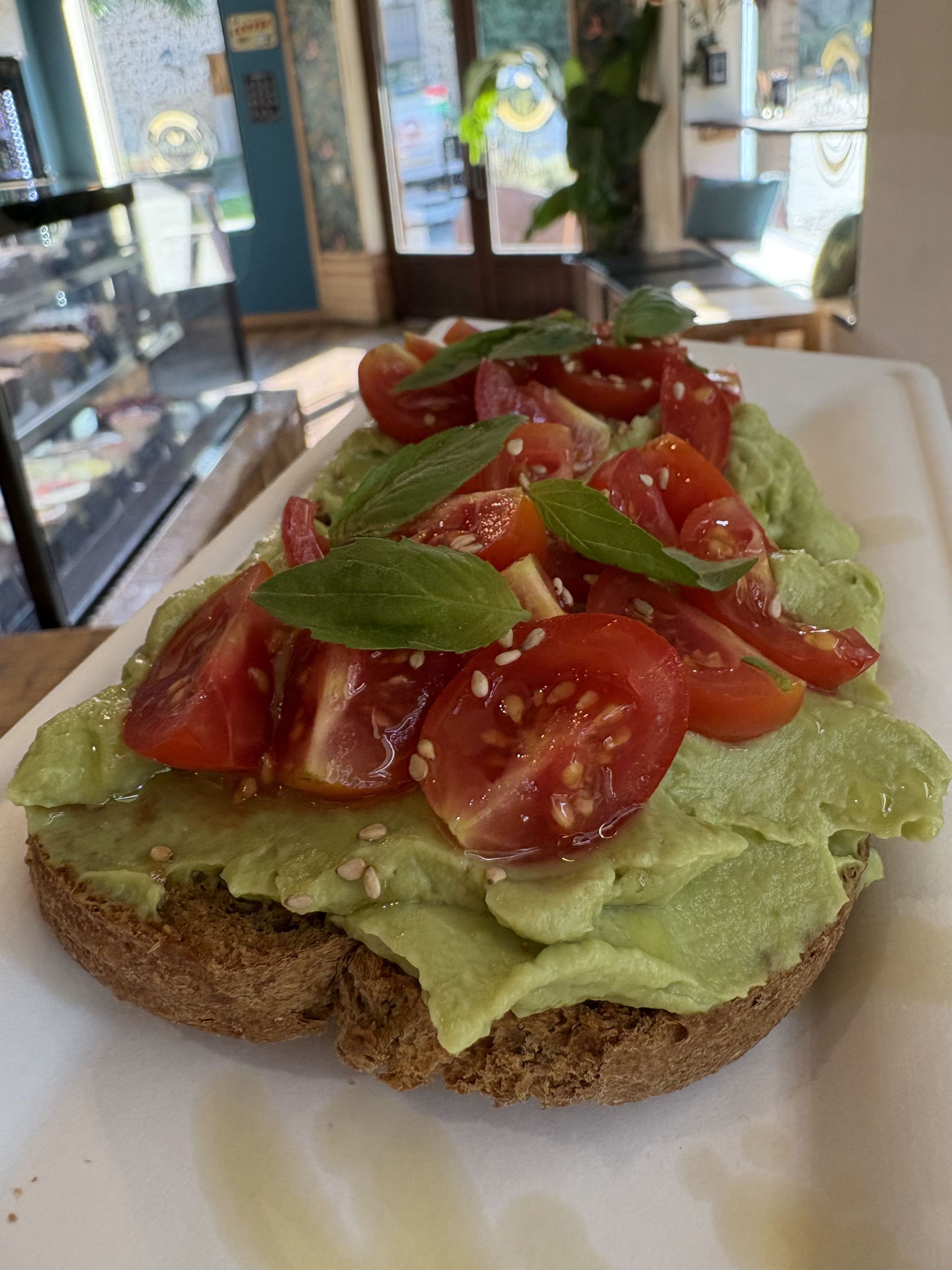 Tostada de aguacate cubierta con tomates, albahaca y semillas de sésamo en un plato blanco.