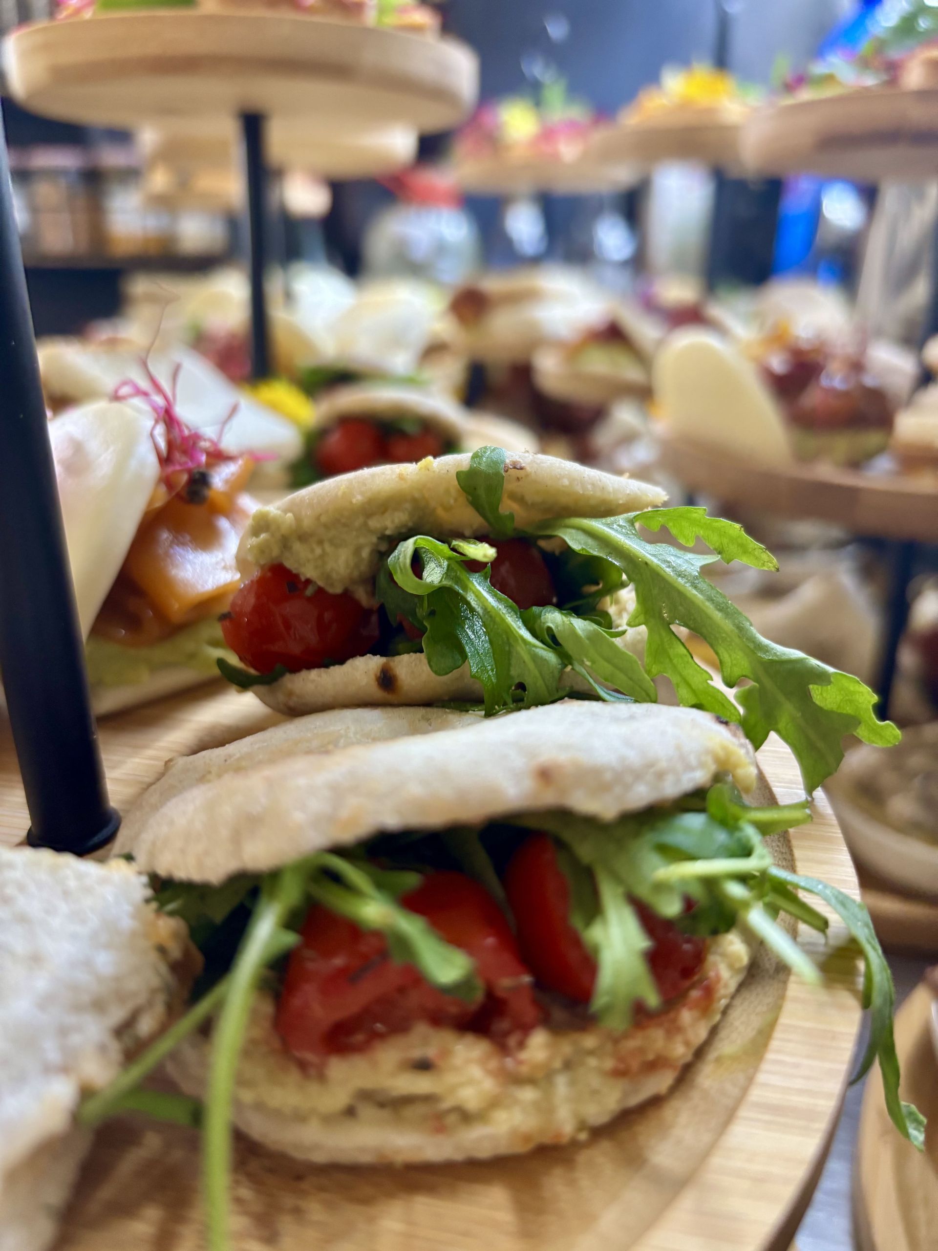 Mini sándwiches con tomate y rúcula en una bandeja escalonada.
