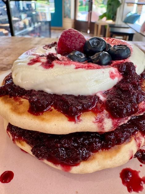 Una pila de panqueques con compota de frutos rojos, crema batida y arándanos en un plato en una cafetería.