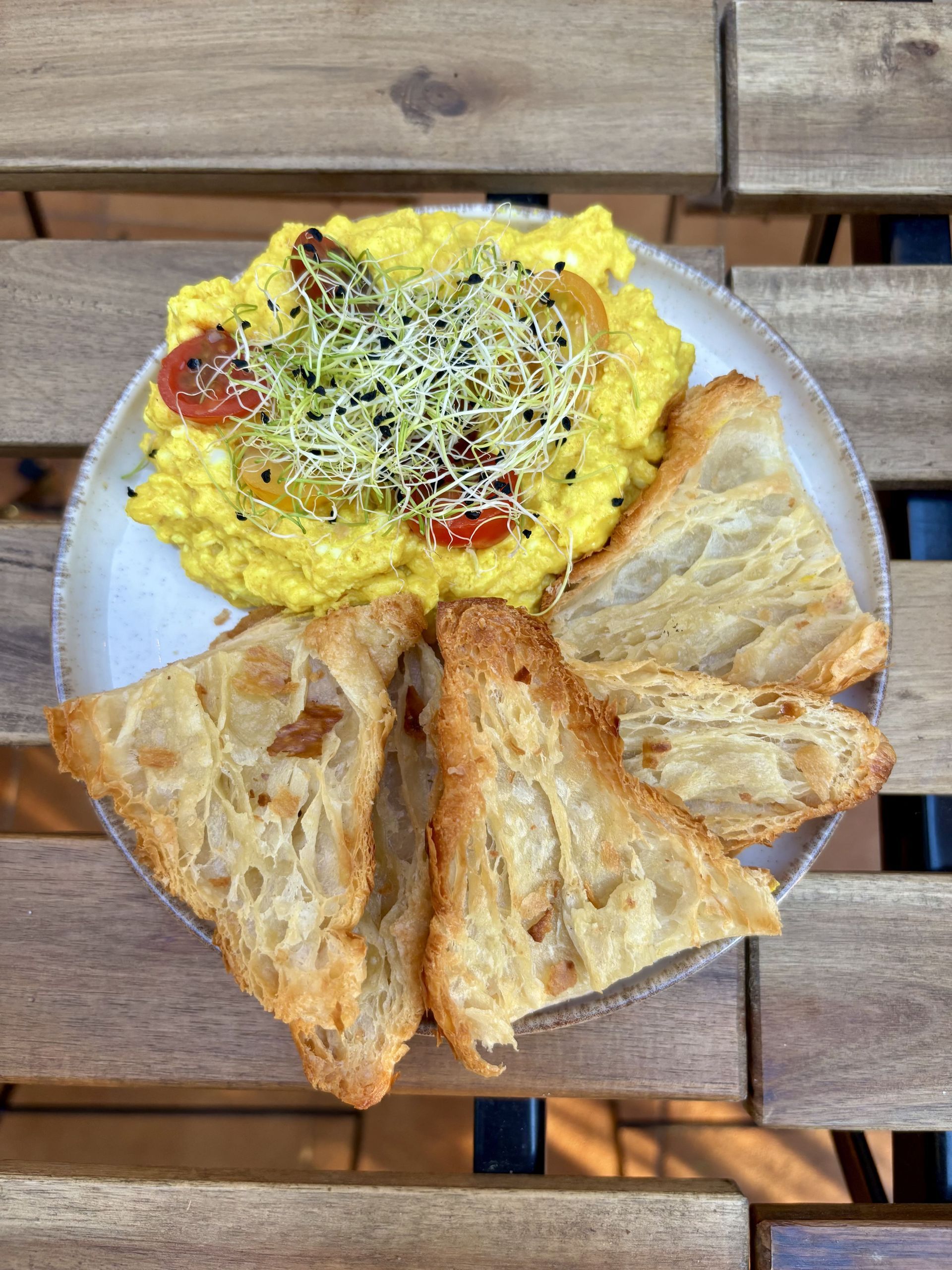 Huevos revueltos con coles y tomates, servidos con pan tostado en un plato. Mesa de madera.