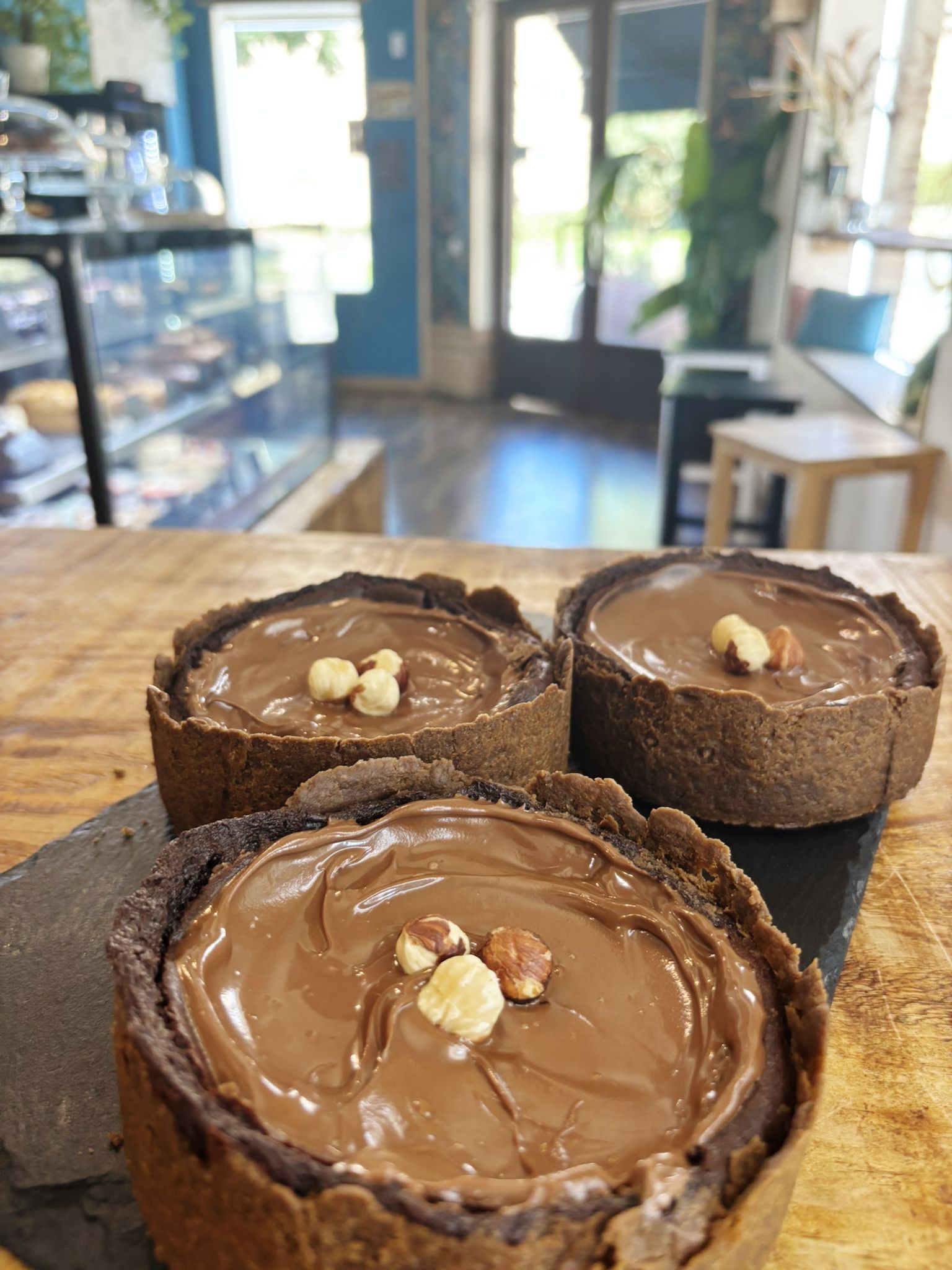 Tres tartas de chocolate con cobertura de avellanas, sobre una mesa de madera en un café.
