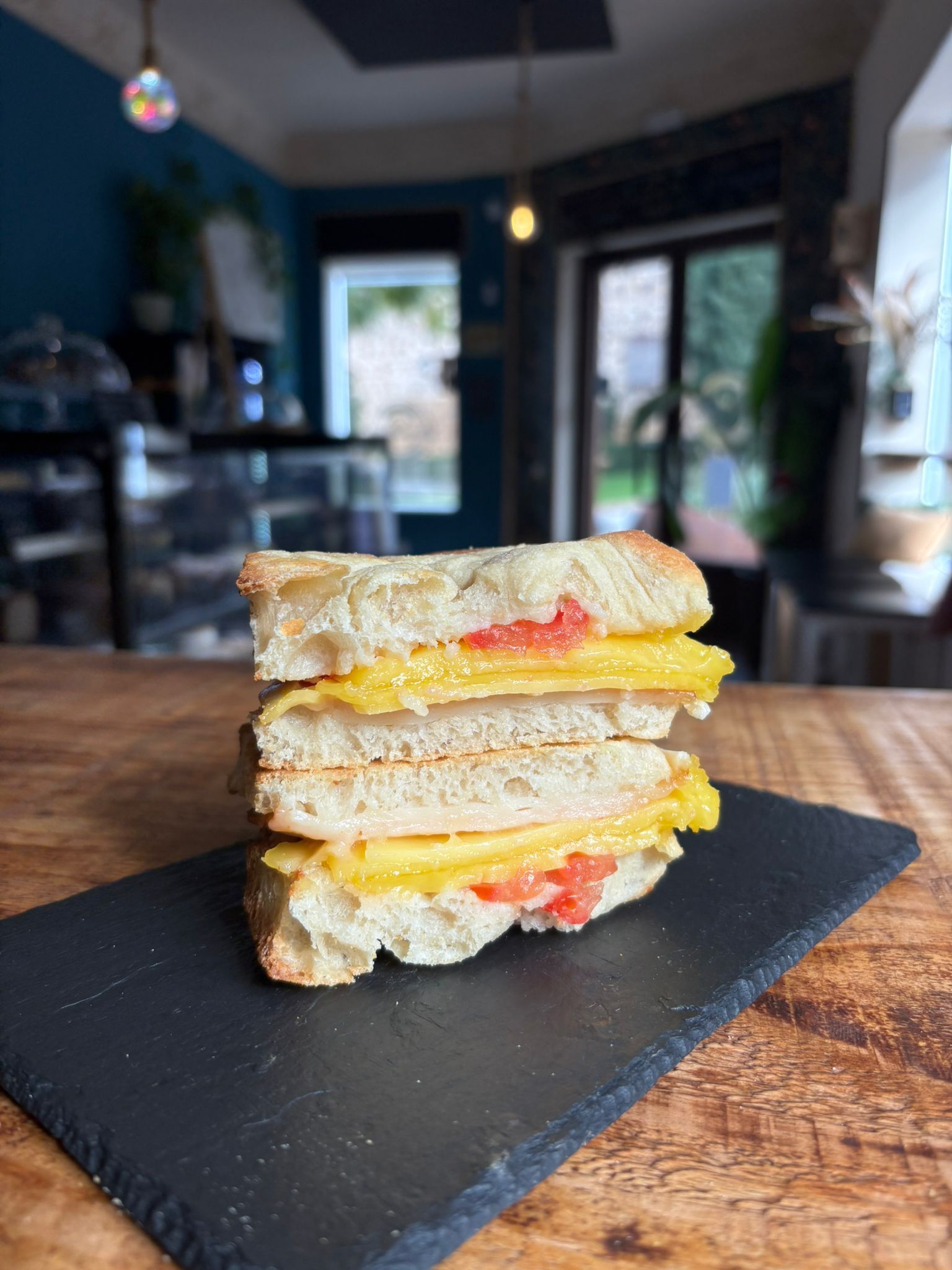 Sándwich de queso a la parrilla sobre una pizarra negra, ambiente de cafetería.