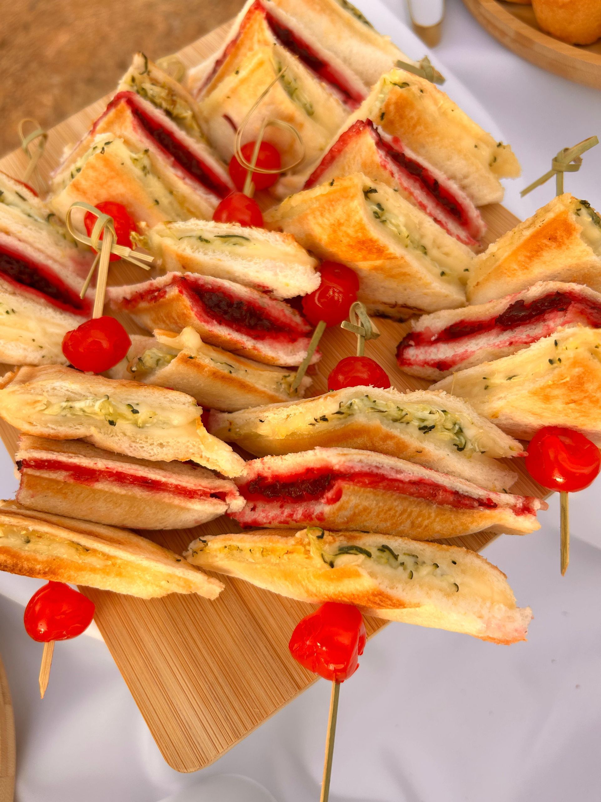 Sándwiches variados en exposición, algunos con relleno rojo, ensartados con tomates cherry.