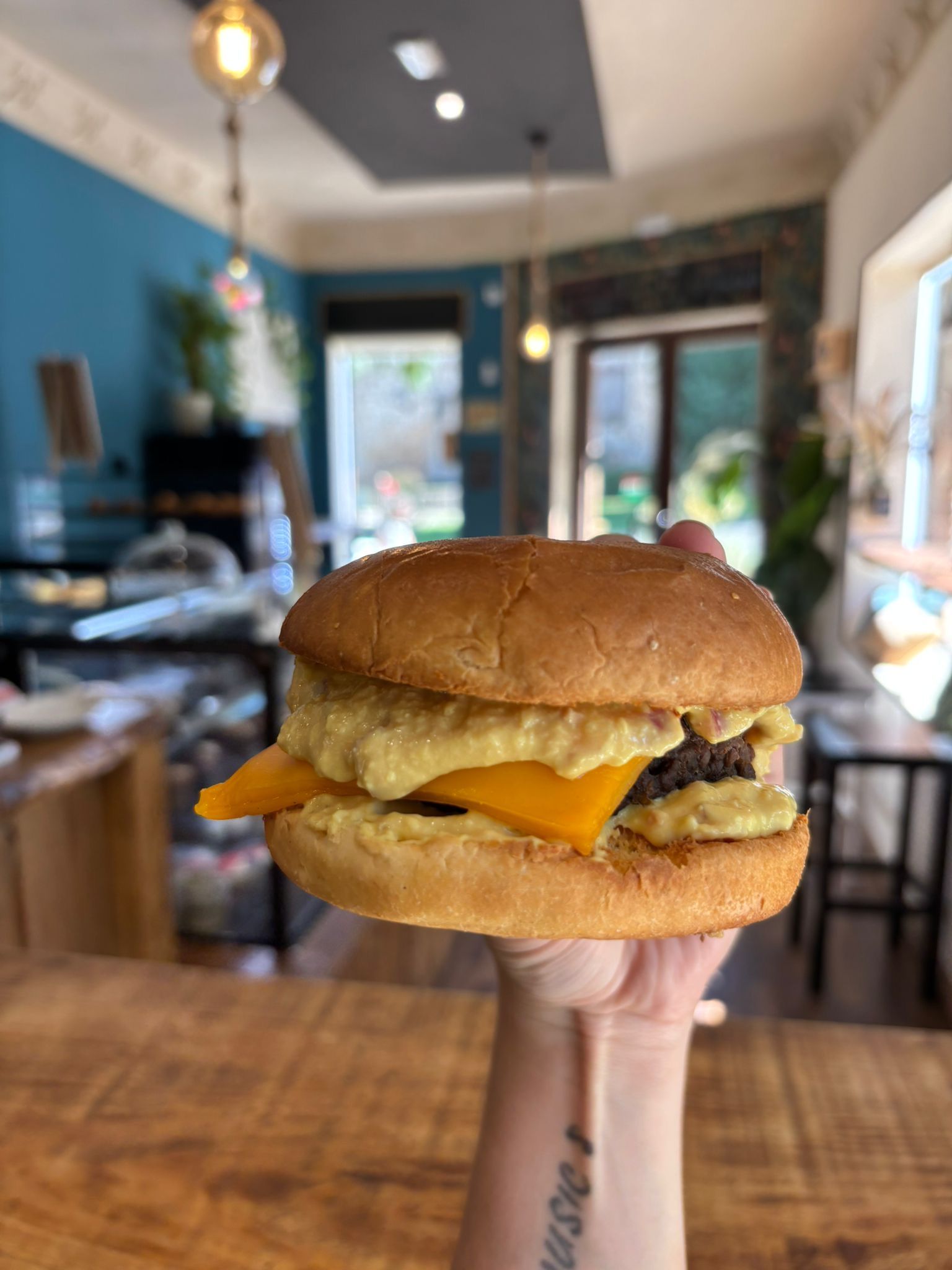 Mano sosteniendo una hamburguesa con queso, salsa y una hamburguesa oscura