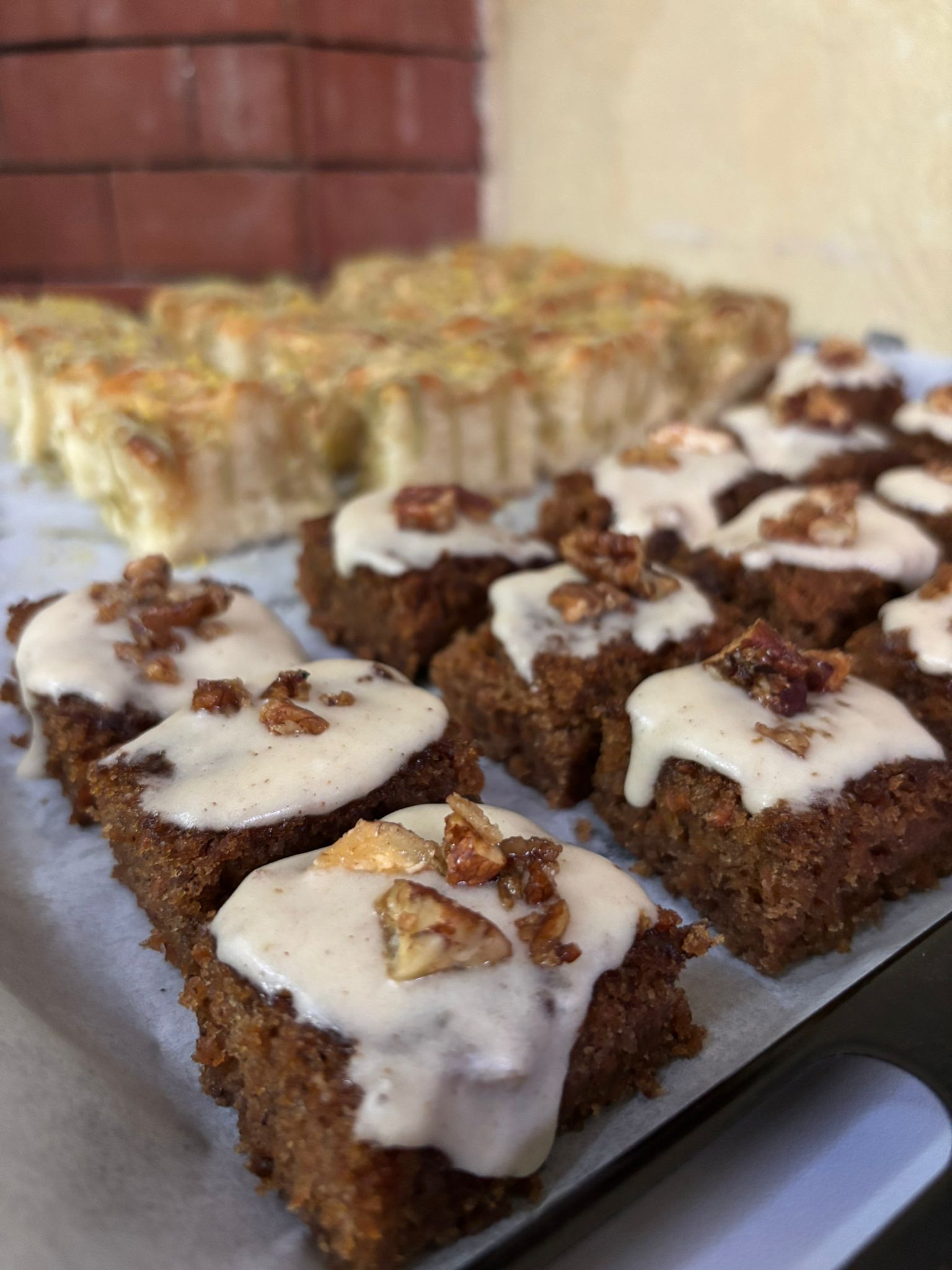 Bandeja de bocaditos cuadrados de pastel de zanahoria glaseado cubierto con nueces y una quiche rectangular.