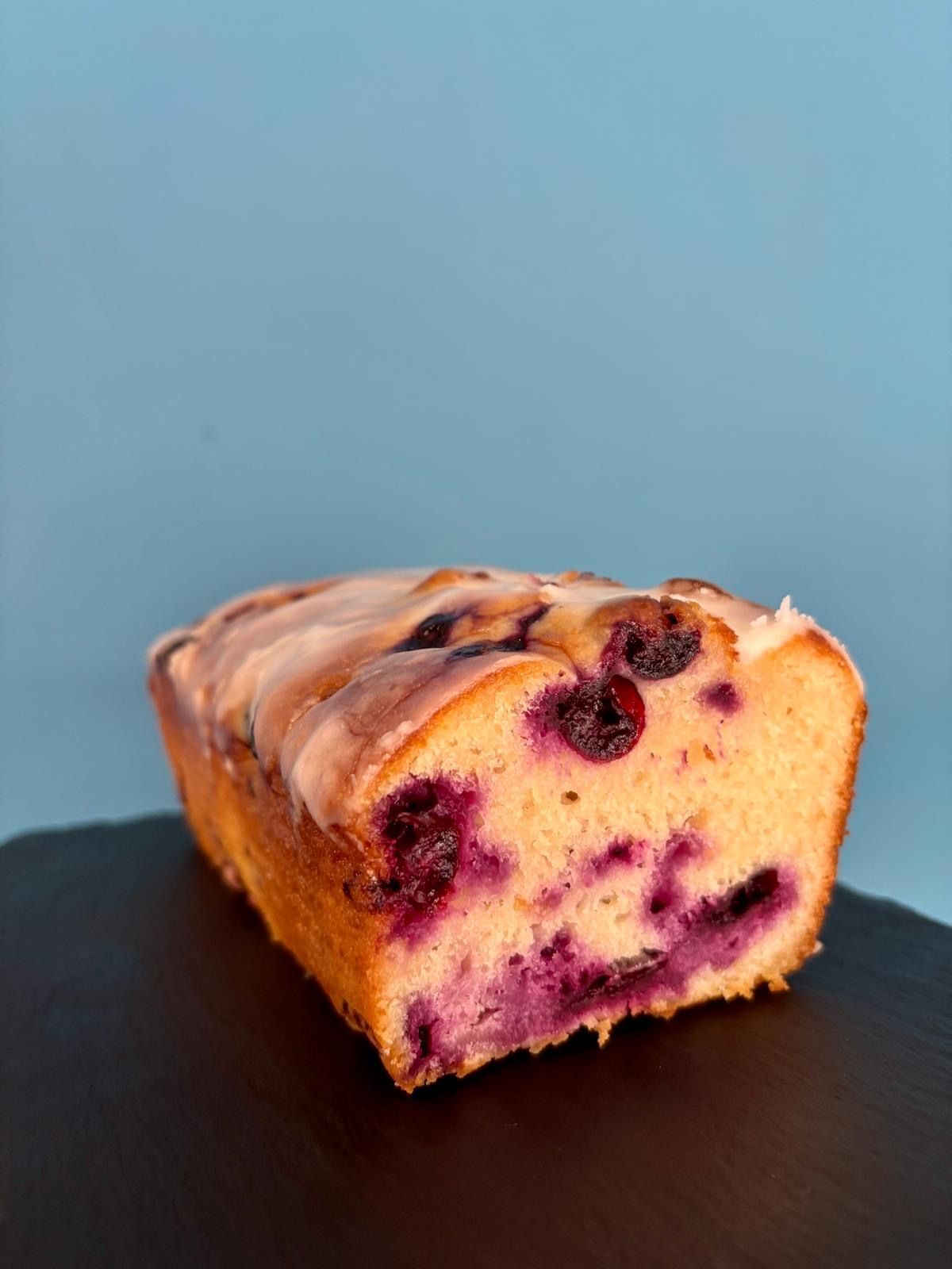 Bizcocho de arándanos sobre una superficie negra sobre un fondo azul, glaseado.
