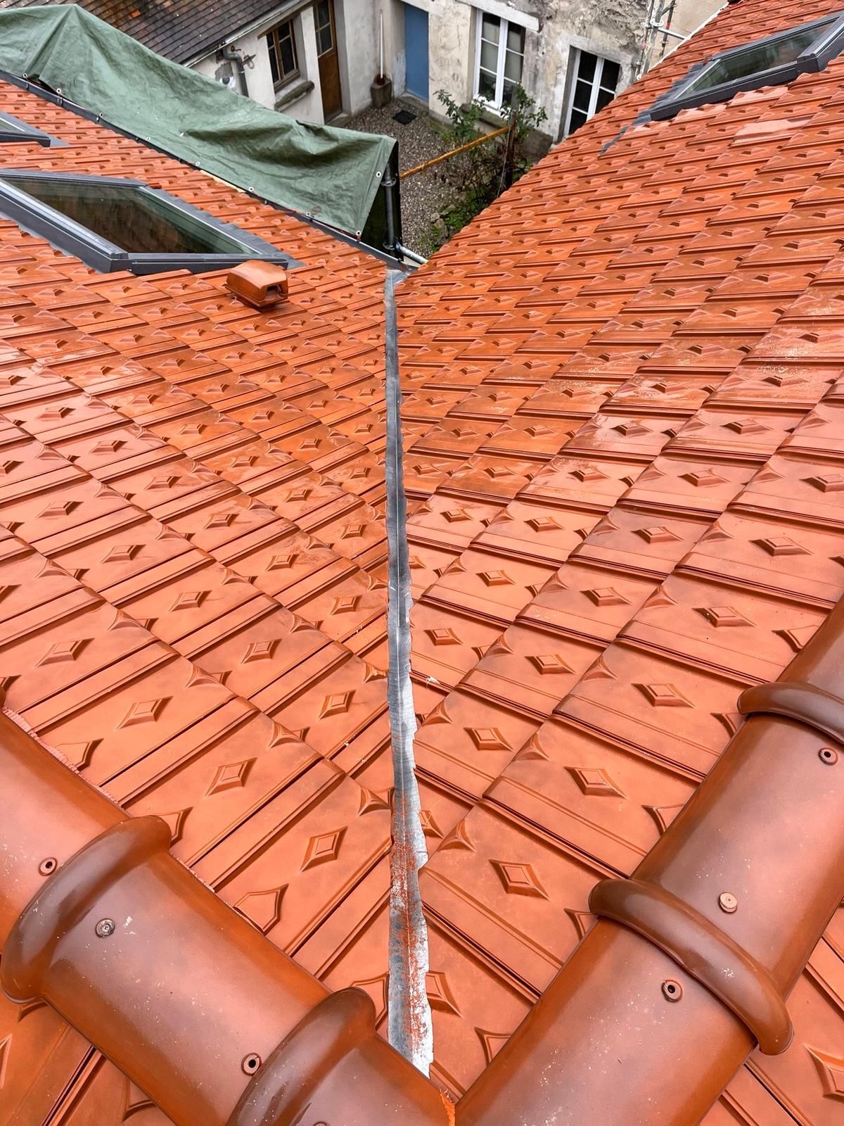 Les toits de tuiles orange se rejoignent au niveau d'une gouttière centrale. Des gouttières marron bordent le toit.