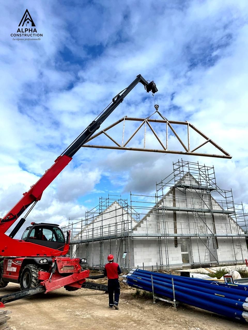 Une grue rouge soulève une ferme de toit sur un bâtiment en construction.