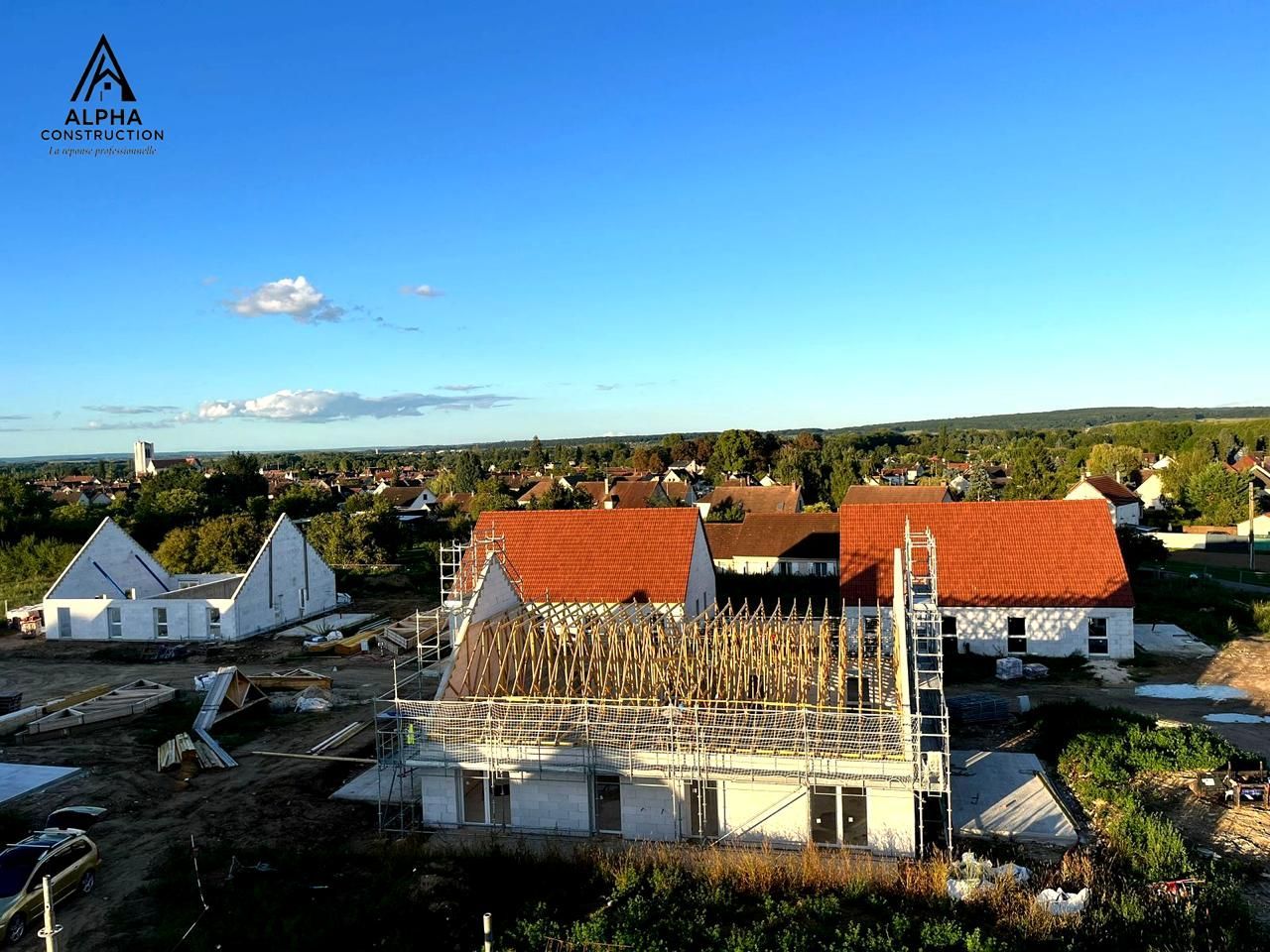 Maisons en construction avec des toits rouges sur fond de ciel bleu, dans un cadre rural.