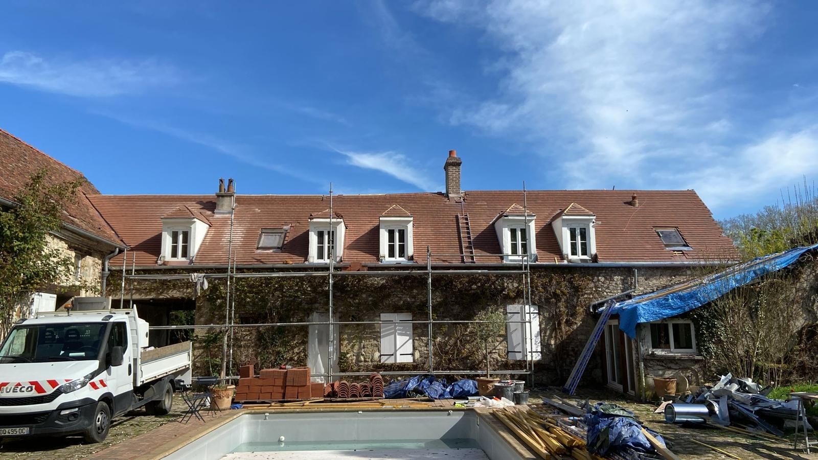 Maison en construction avec échafaudage, piscine et camion de travail par une journée ensoleillée.