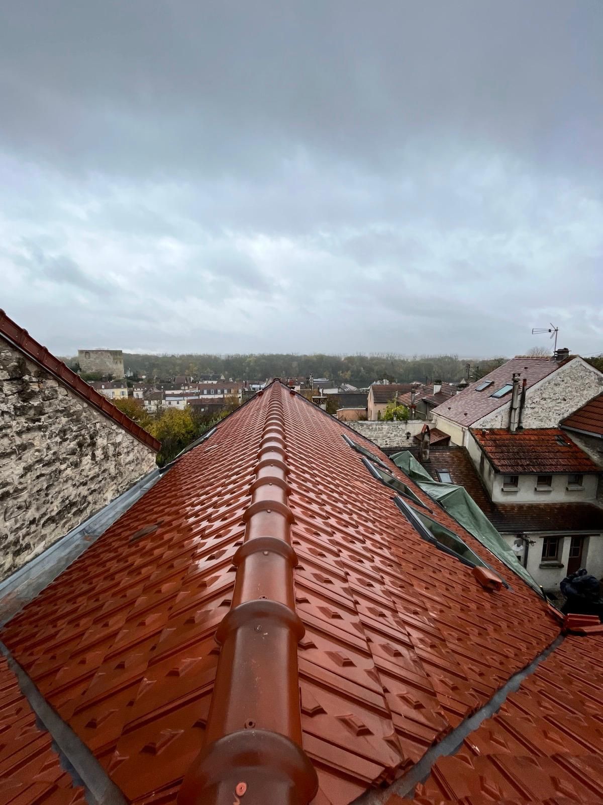 Toit en tuiles rouges par temps nuageux, surplombant une ville avec des arbres et des bâtiments.