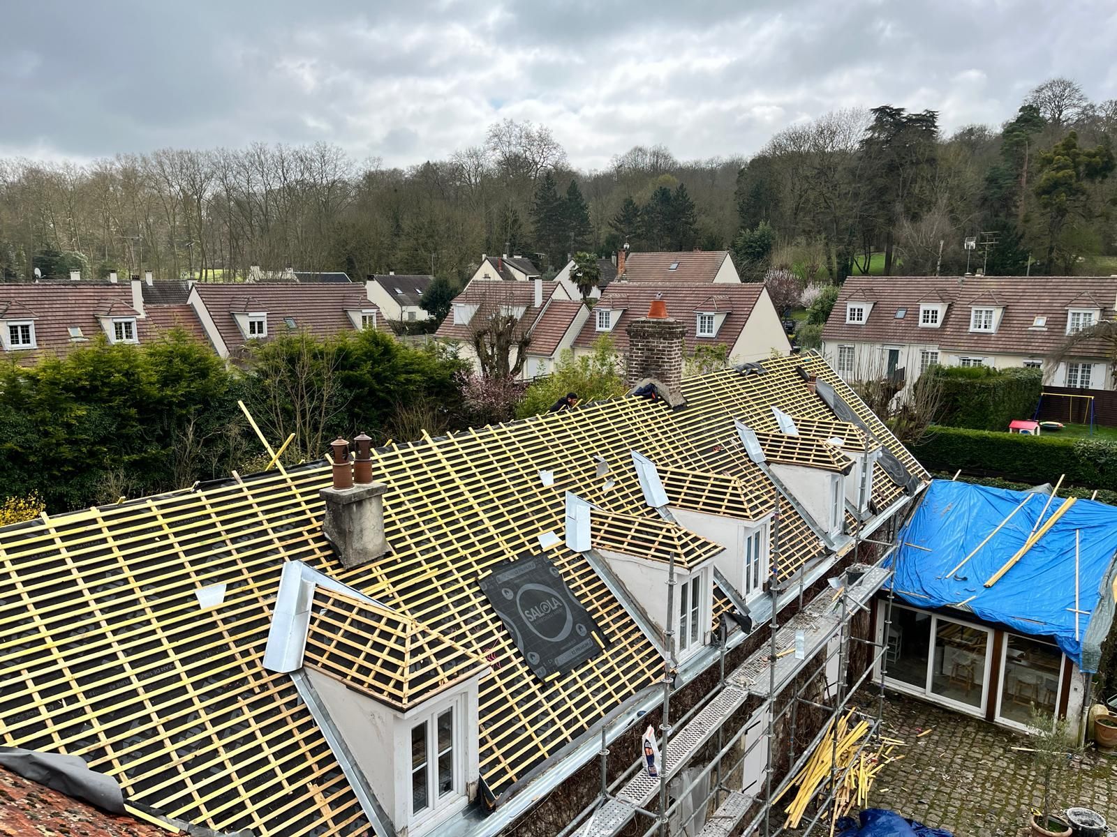 Toiture avec lattes de bois neuves. Bâtiments en arrière-plan, ciel nuageux.