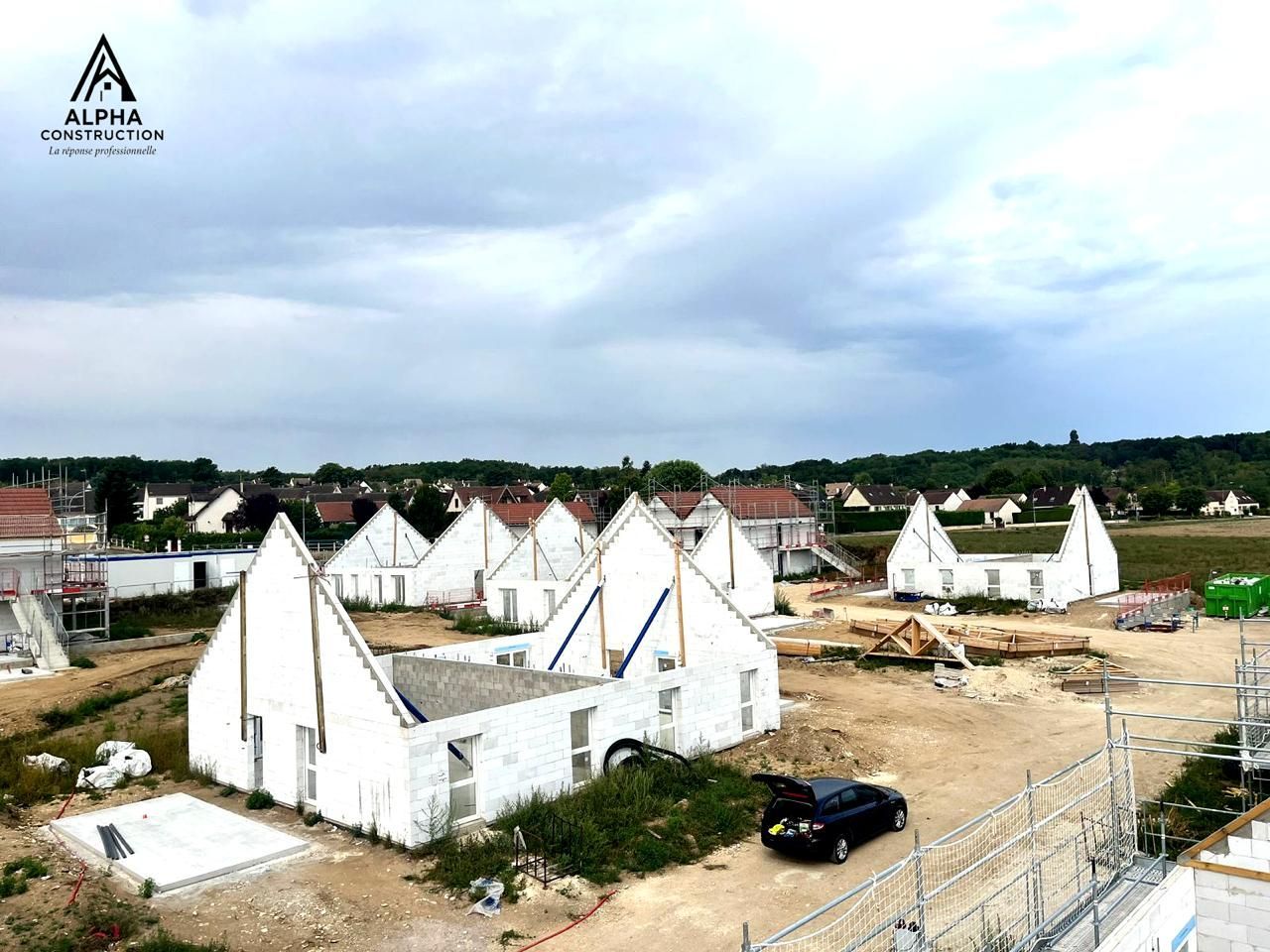 Chantier de construction avec des maisons blanches inachevées sous un ciel nuageux.