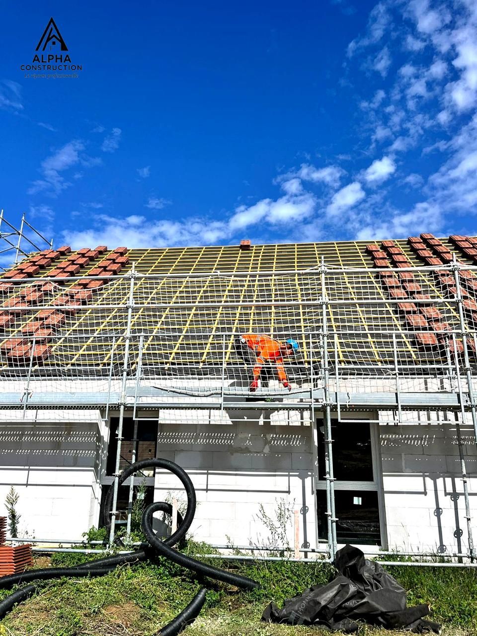 Ouvrier du bâtiment sur un échafaudage installant des tuiles de toit sous un ciel bleu.