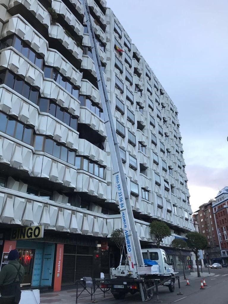 Un camión con una escalera adjunta está estacionado frente a un edificio alto.