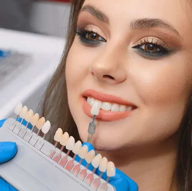 Una mujer sostiene una tabla de colores de dientes frente a su boca.