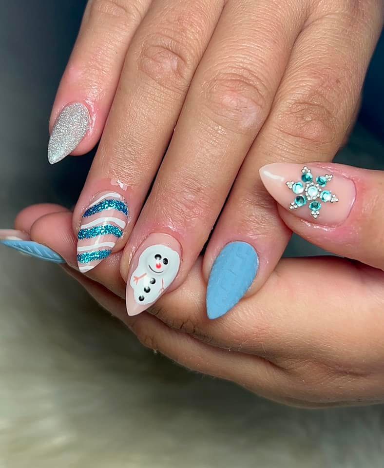 Uñas con forma de almendra decoradas con motivos invernales festivos, como un muñeco de nieve, rayas azules brillantes y un copo de nieve.