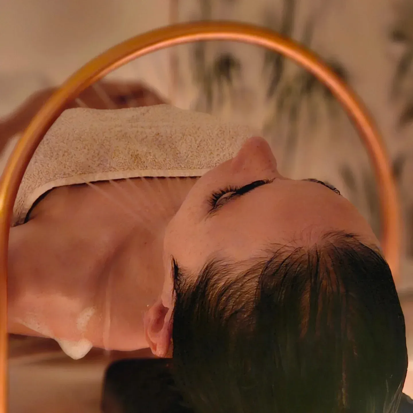 Una persona recibe un relajante tratamiento de spa craneal, recostada con una toalla que le cubre el pecho bajo una luz circular.