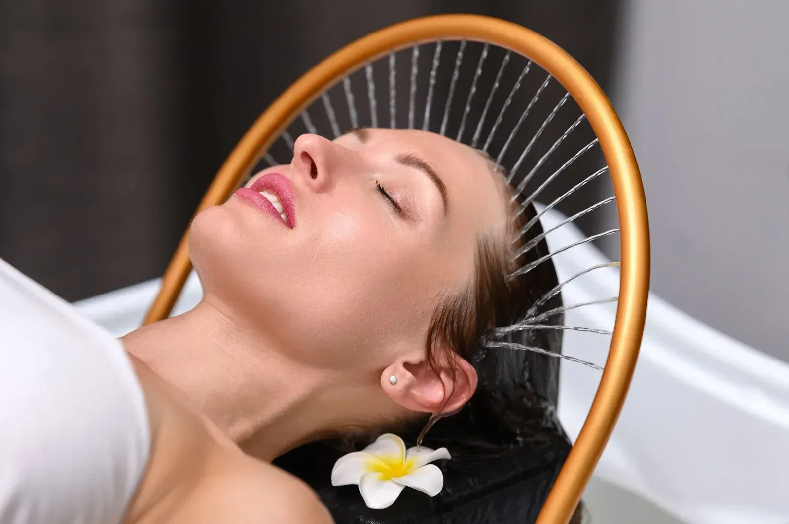 Una persona se relaja con los ojos cerrados mientras una fuente circular rocía agua suavemente sobre su cabello en un ambiente de spa.