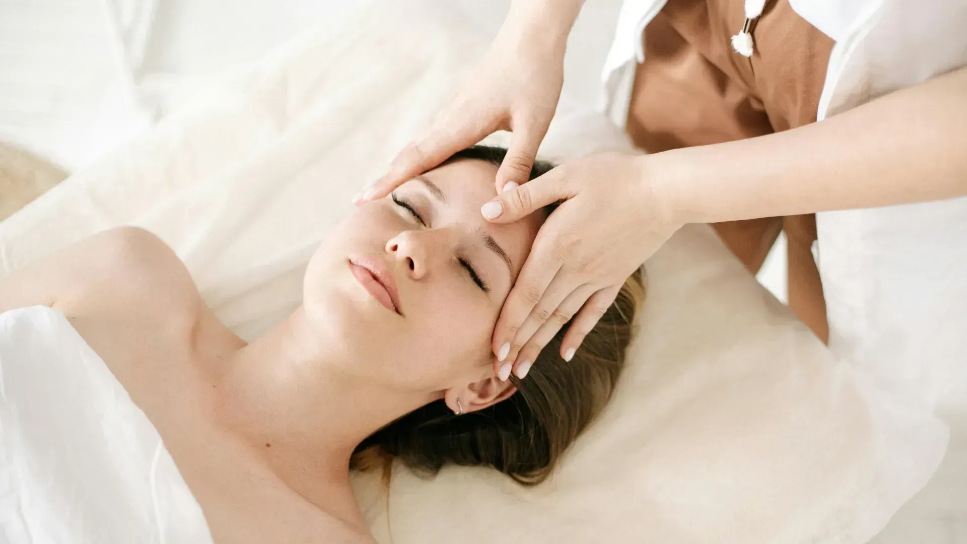Un terapeuta realiza un masaje facial relajante a una persona tumbada en una camilla de tratamiento.