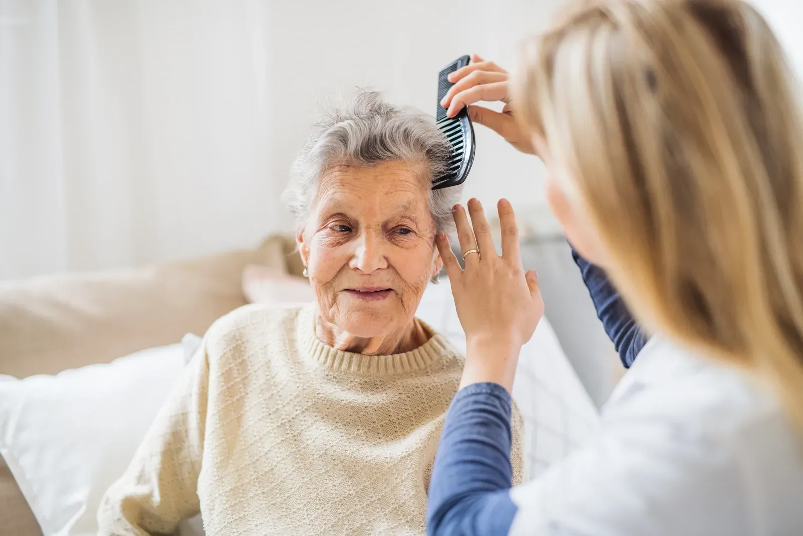 Eine Krankenschwester kämmt einer älteren Frau die Haare.