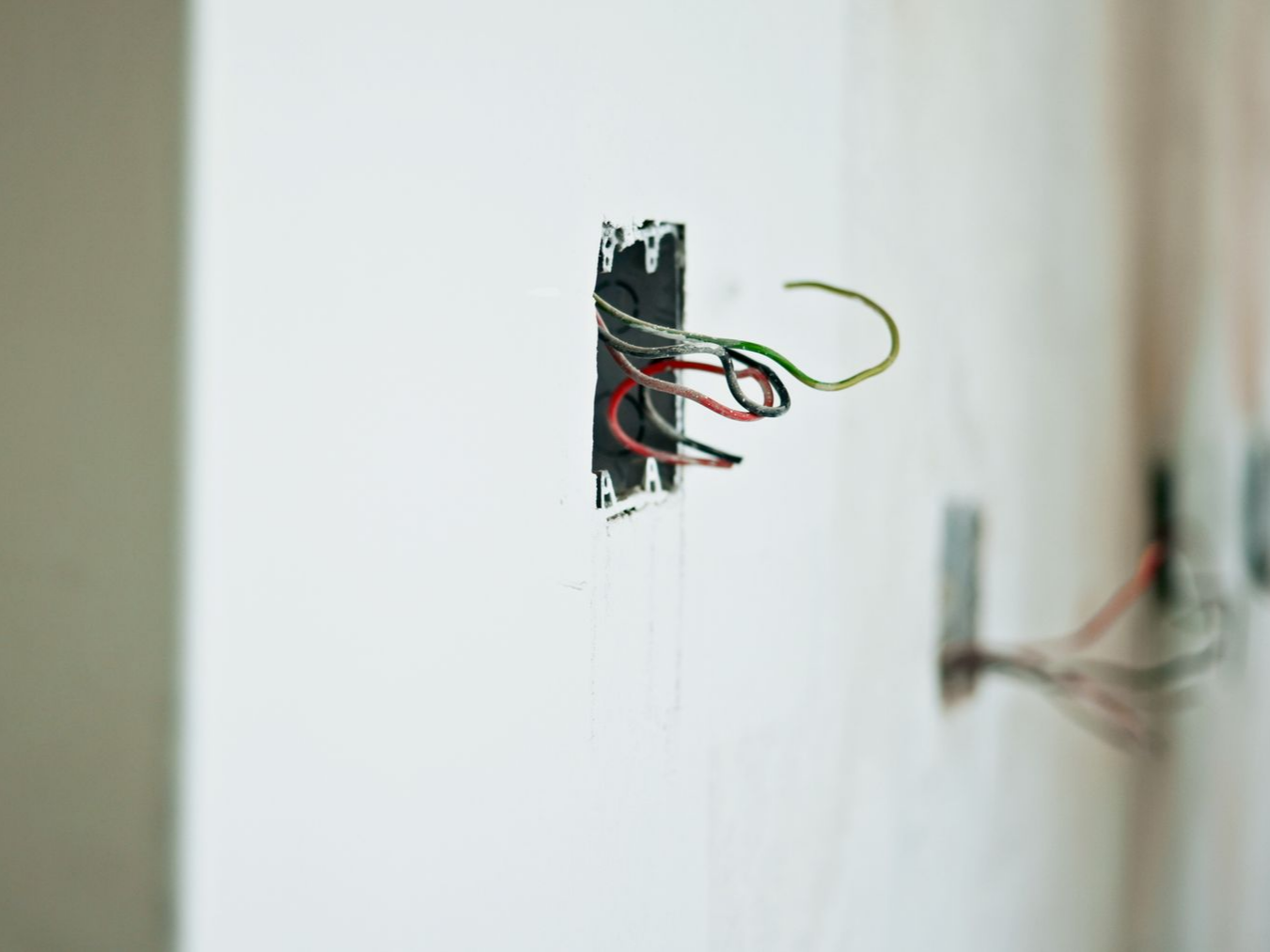 Fils électriques dépassant d'une prise inachevée dans un mur blanc.