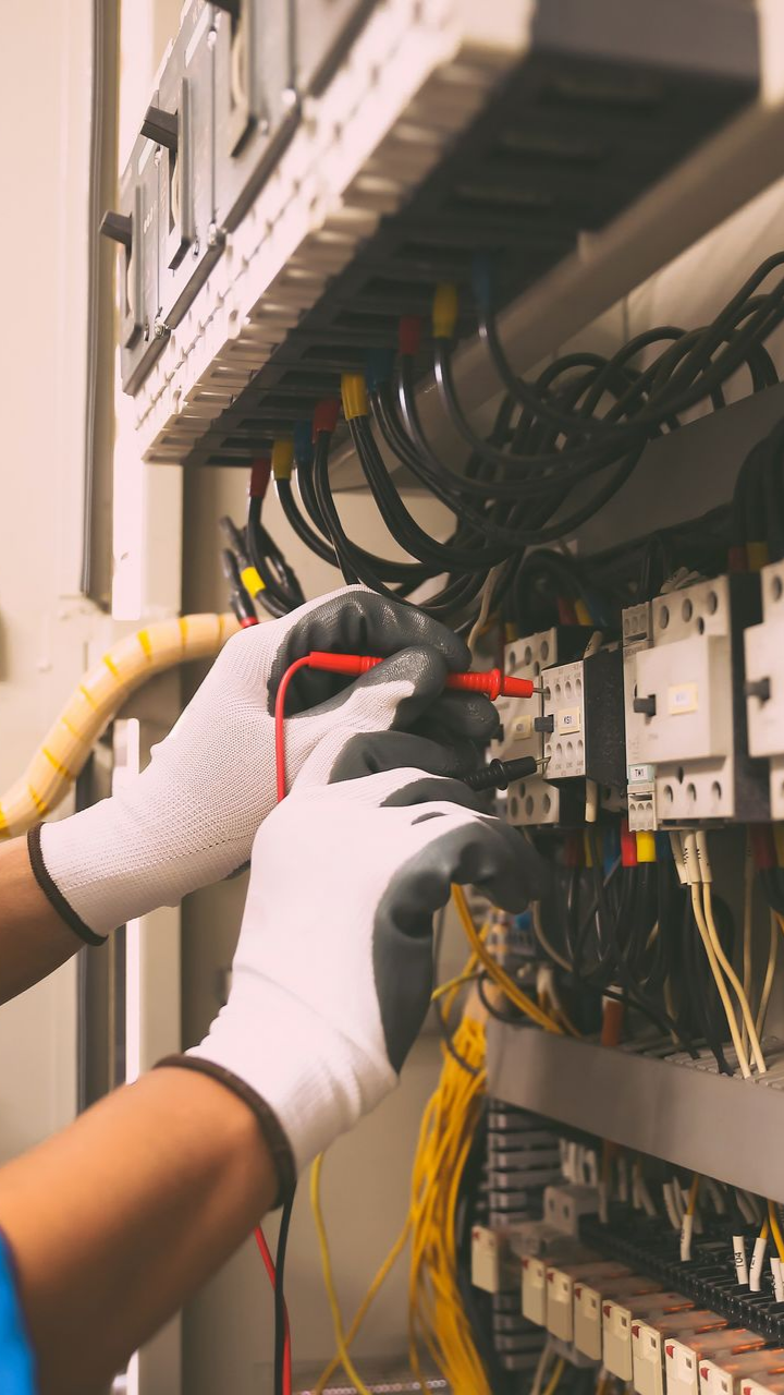 Des mains portant des gants testent le panneau électrique avec un multimètre.
