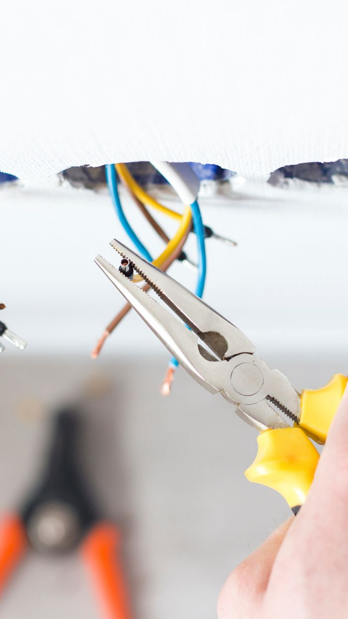 Main utilisant une pince pour travailler sur des fils électriques exposés dans un mur.