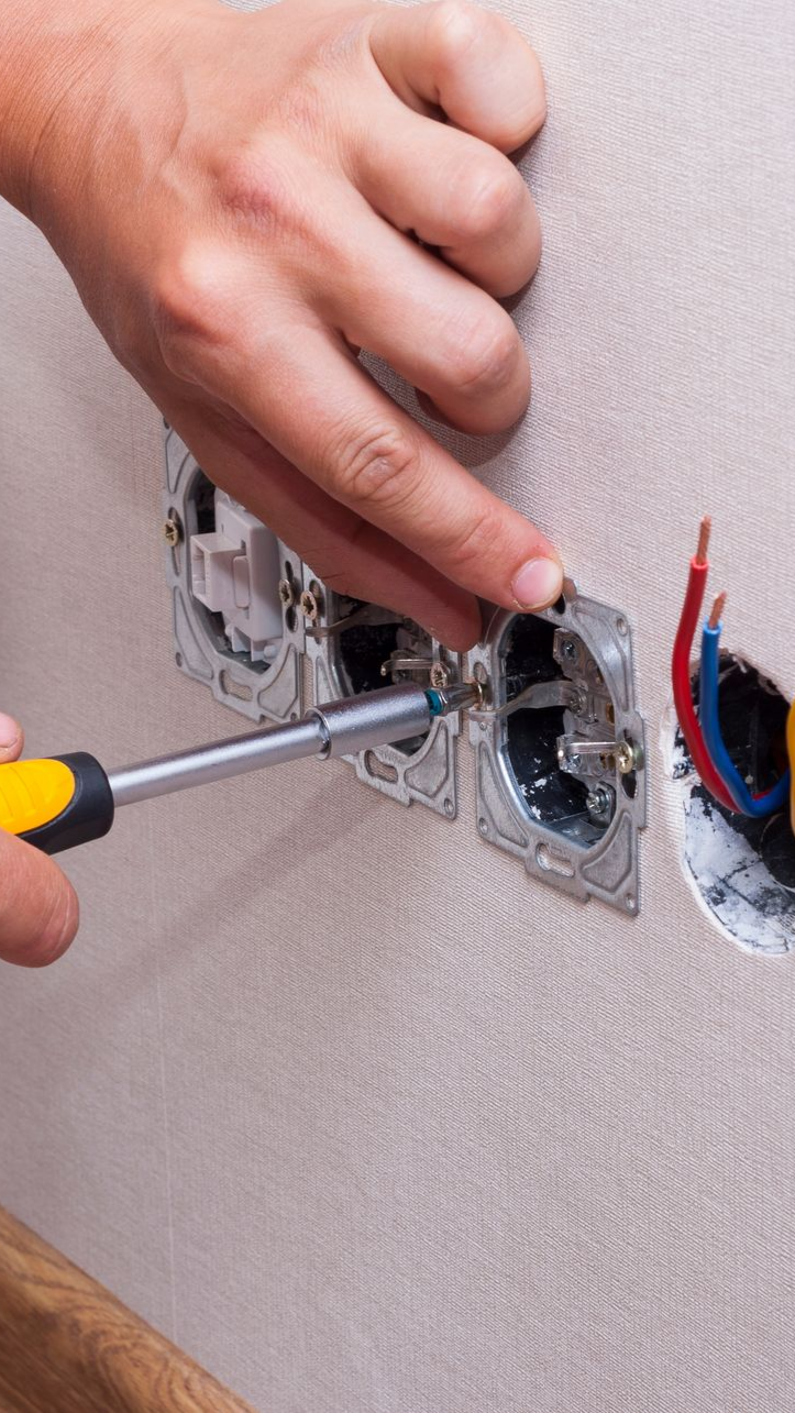 Personne utilisant un tournevis pour installer une prise électrique sur un mur, avec des fils exposés.