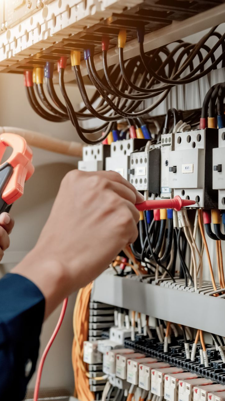 Électricien testant le câblage électrique dans un panneau de contrôle avec un multimètre.