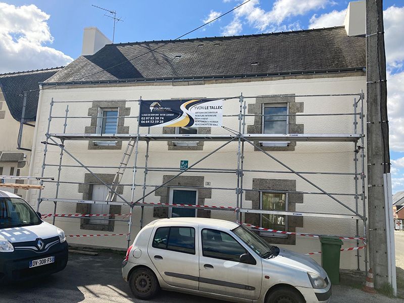 Bâtiment avec échafaudage ; rénovation extérieure. Maison à deux étages, façade claire, toit foncé. Voitures garées devant.